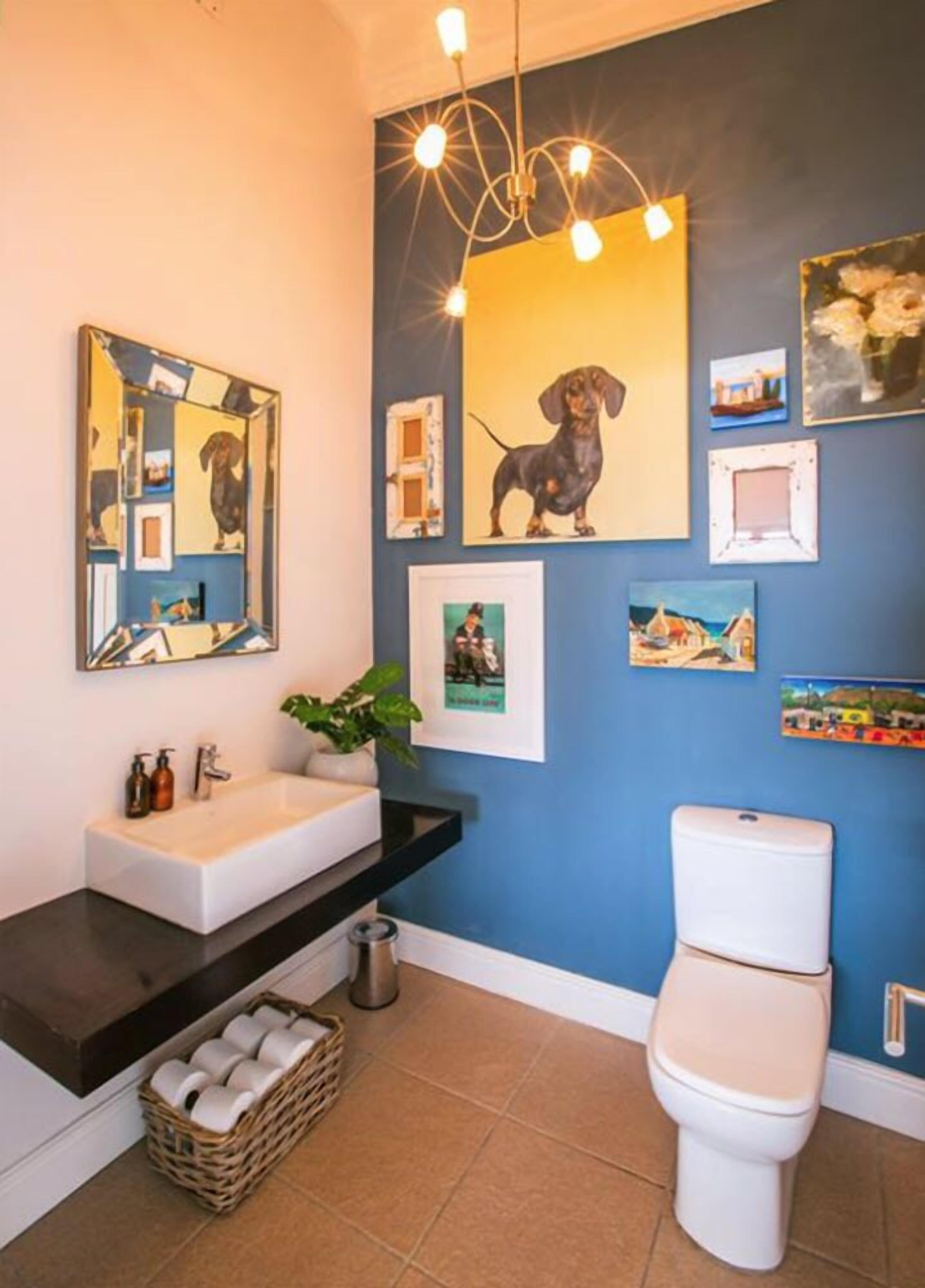 A bathroom with a white sink, black countertop, and a white toilet. There are framed pictures on the wall, a hanging light fixture, and a mirror above the sink.