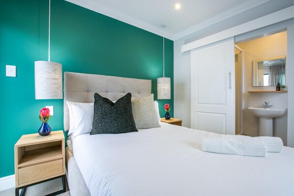 A modern bedroom with a teal wall, a white bed, and a white door leading to a bathroom. - Hout & About Guest House (Cape Town)