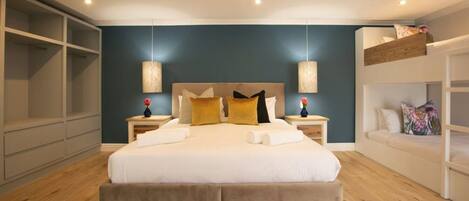 A modern bedroom with a large bed, two bedside tables, a built-in wardrobe, and a bunk bed.