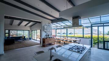 A modern kitchen with a large island, a dining area with a view, and a living room with a sofa and large windows.