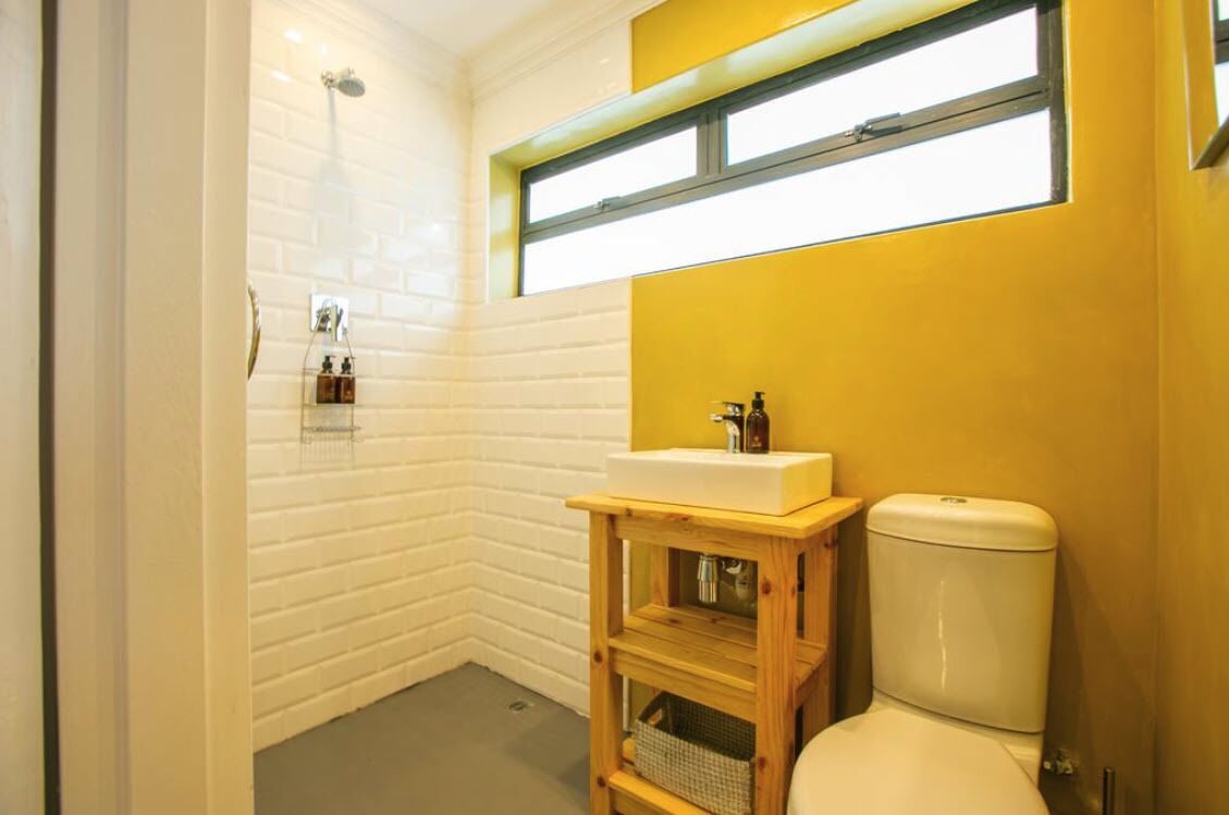 A bathroom with a white tiled shower, a wooden vanity with a sink, and a toilet.