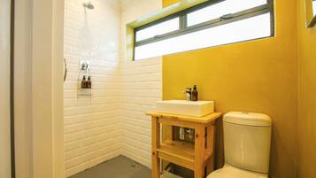 A bathroom with a white tiled shower, a wooden vanity with a sink, and a toilet.