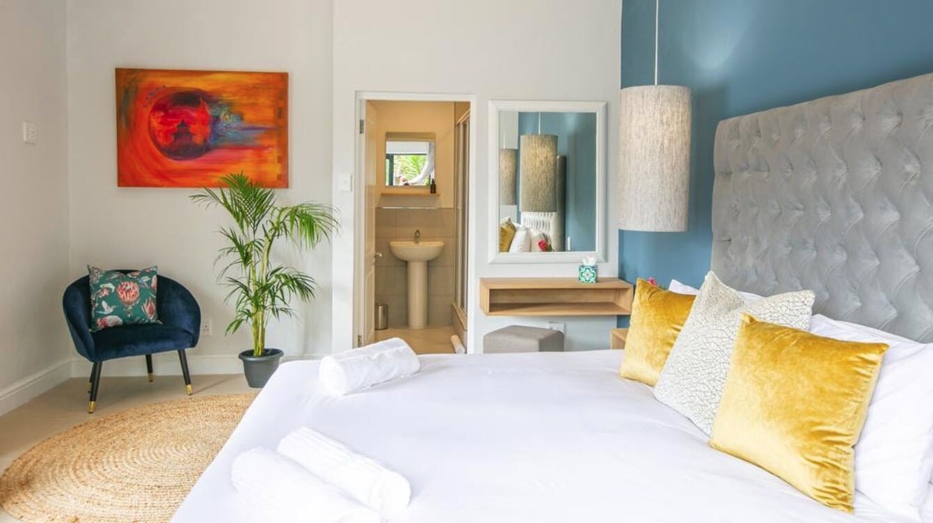 Une chambre à coucher avec un grand lit, une table de chevet, un miroir, un luminaire suspendu et une plante en pot.