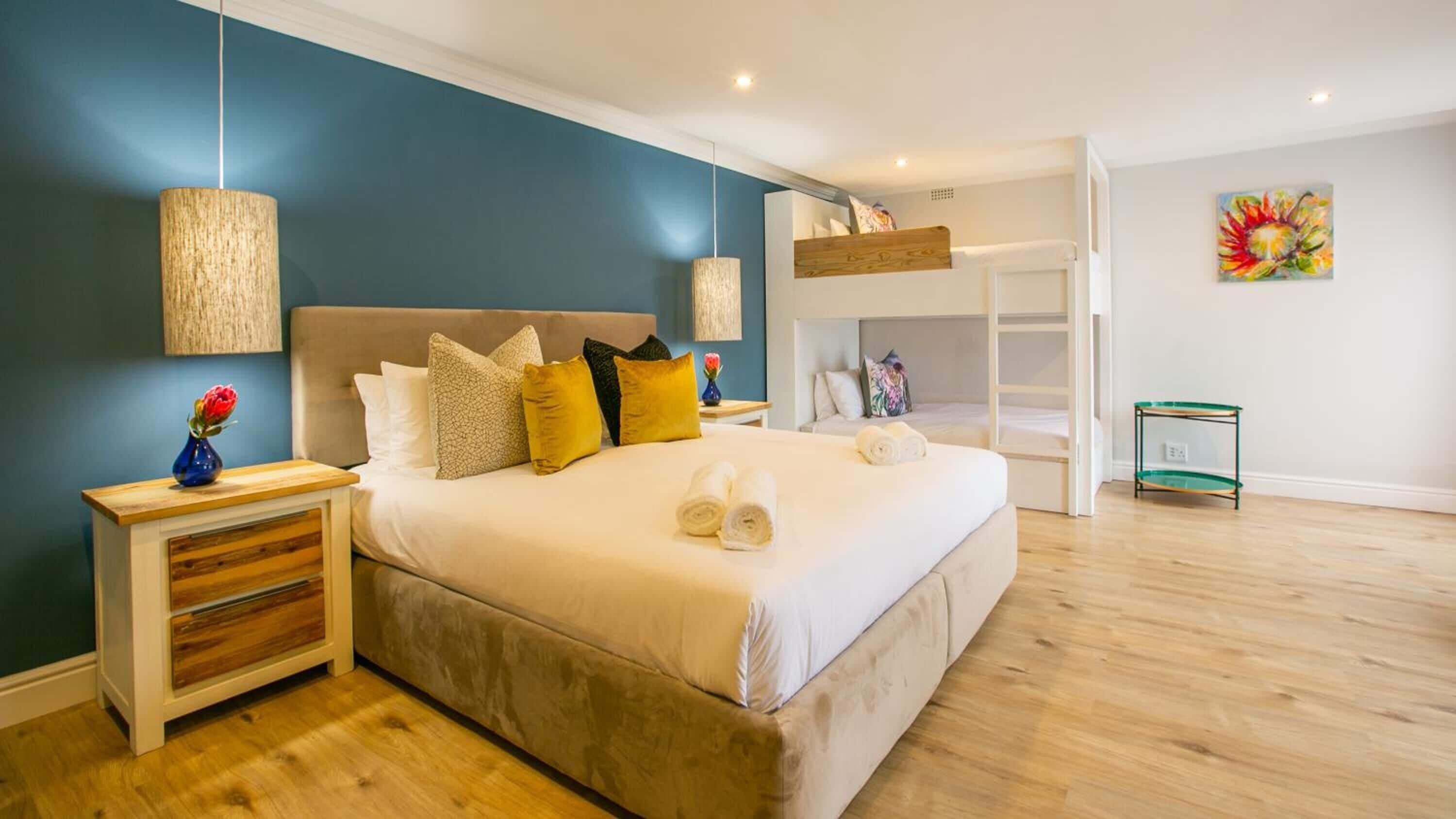 Ein modernes Schlafzimmer mit einem großen Bett, einem Nachttisch, einer Kommode und einem Etagenbett im Hintergrund.