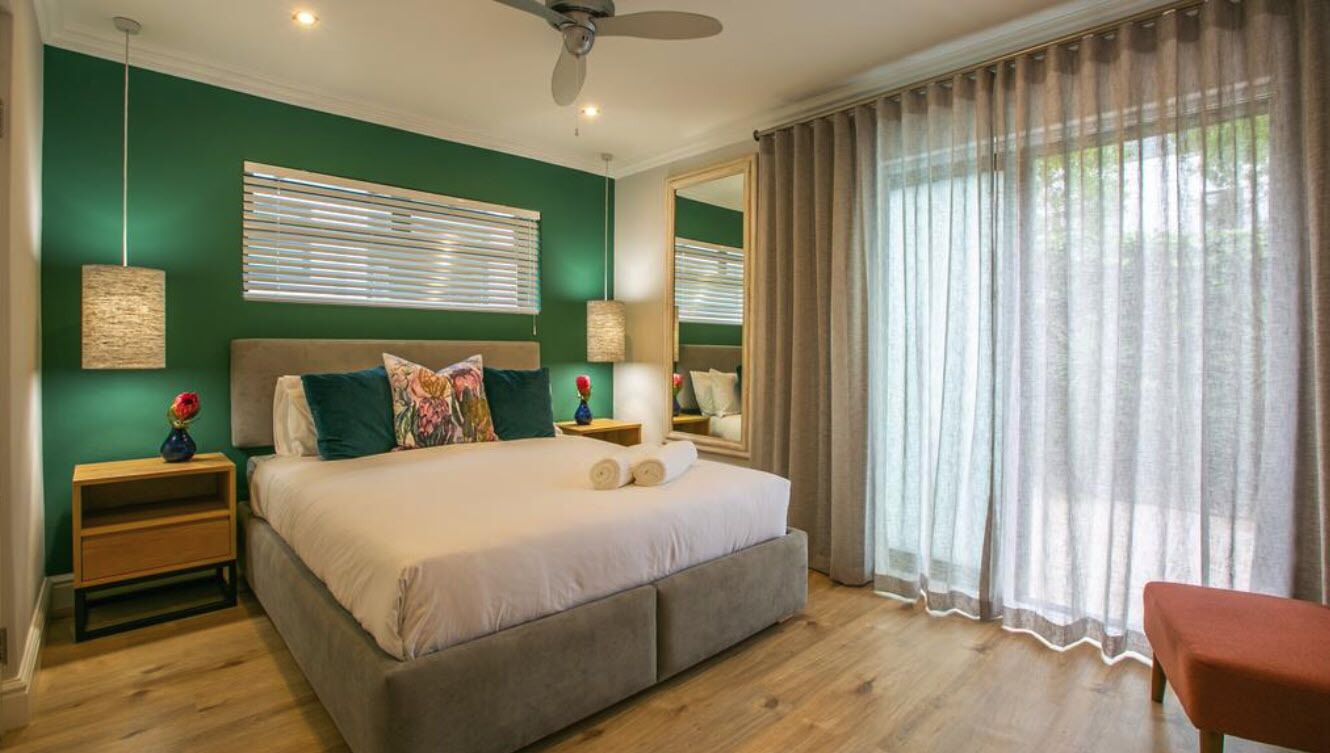 A bedroom with a large bed, two bedside tables, a ceiling fan, and a window with curtains.