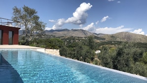A clear swimming pool with a view of mountains and a red building in the background. - Charming villa pool near sea to couple with stay in Italy (Itri)