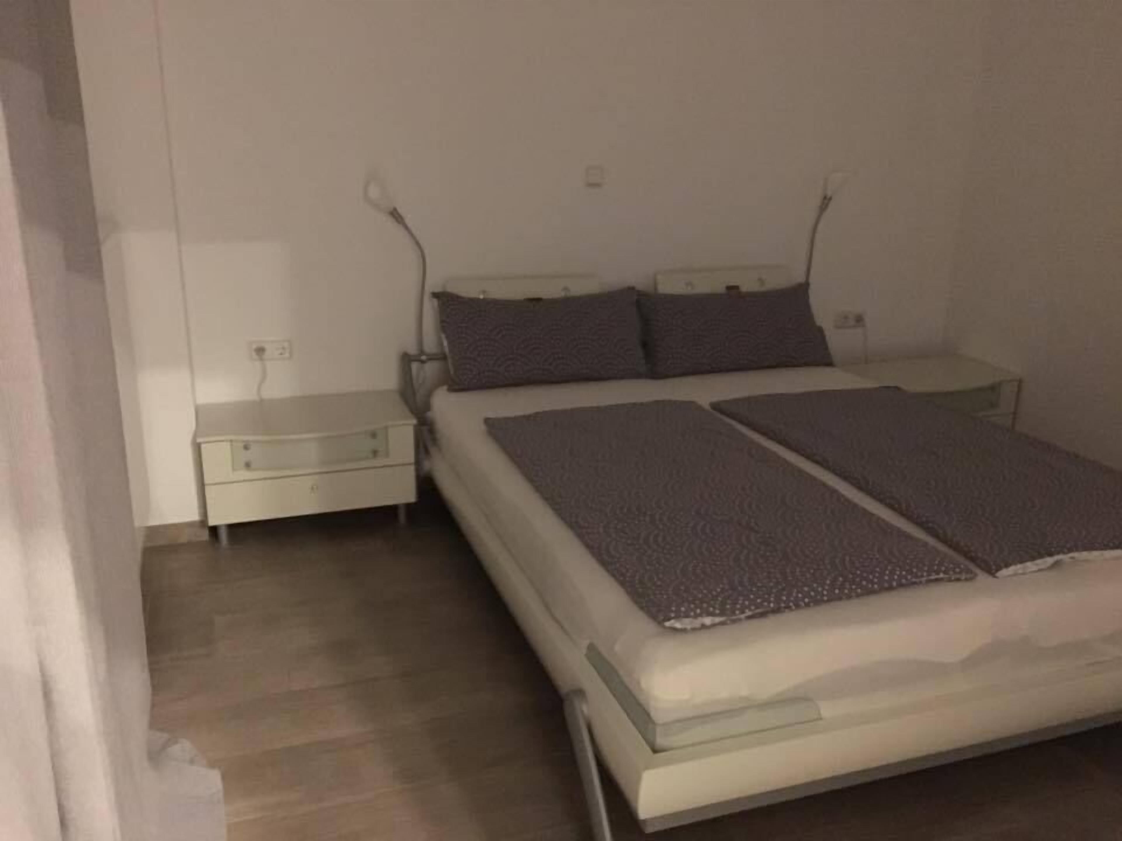 A single-bed room with a wooden floor, a white bedside table, a nightstand, and a bed with a patterned blanket.