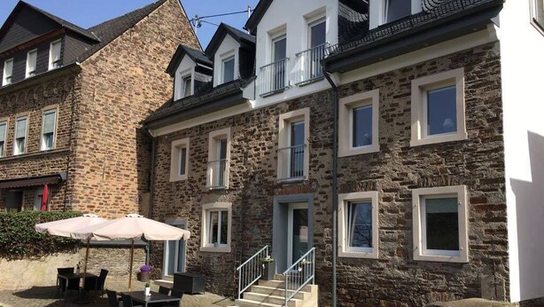 A stone building with a balcony, outdoor seating, and a staircase leading to the entrance. - Apartments am Moselufer (Bruttig-Fankel)