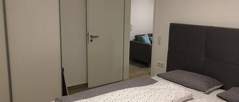 A bedroom with a bed, a wardrobe, and a door leading to another room.