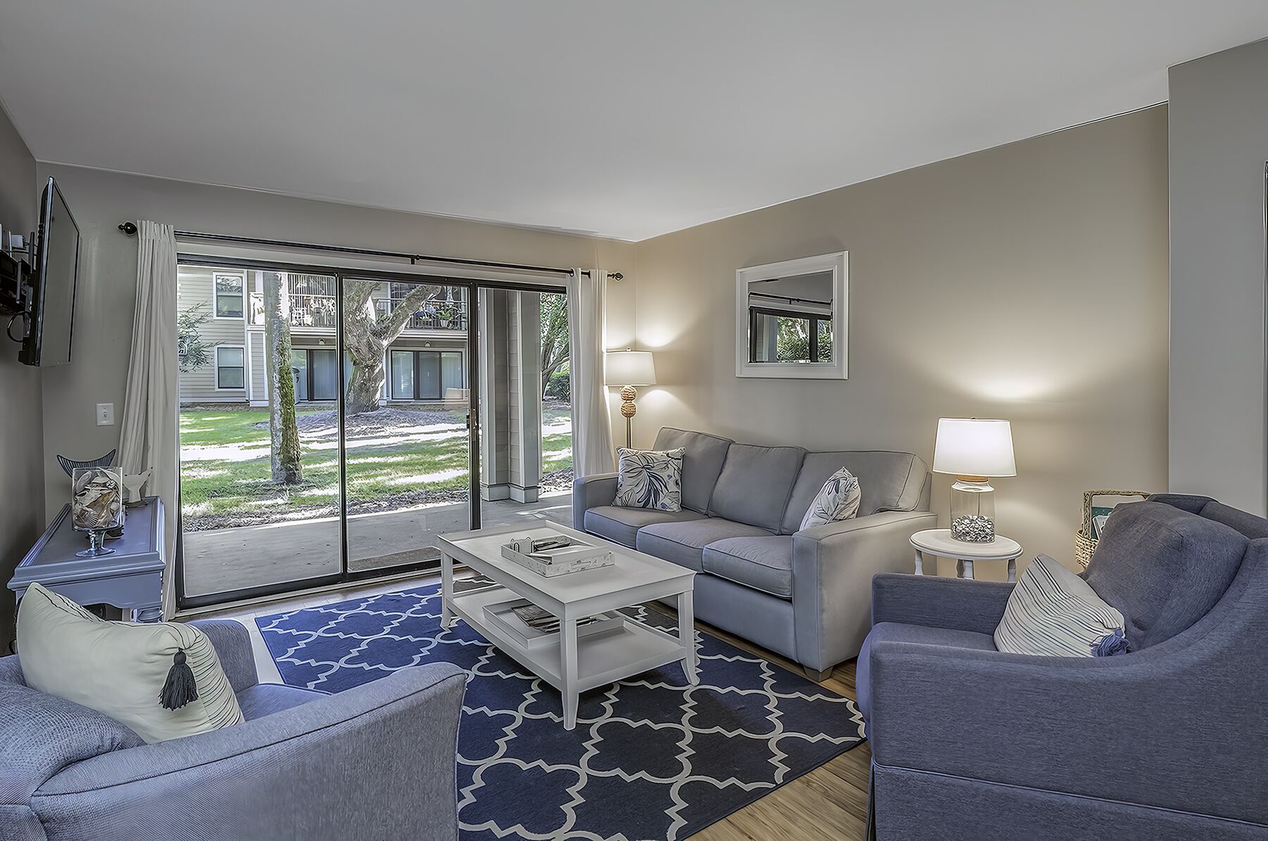 Un salon moderne avec un canapé gris, une table basse blanche et un tapis à motifs bleus.