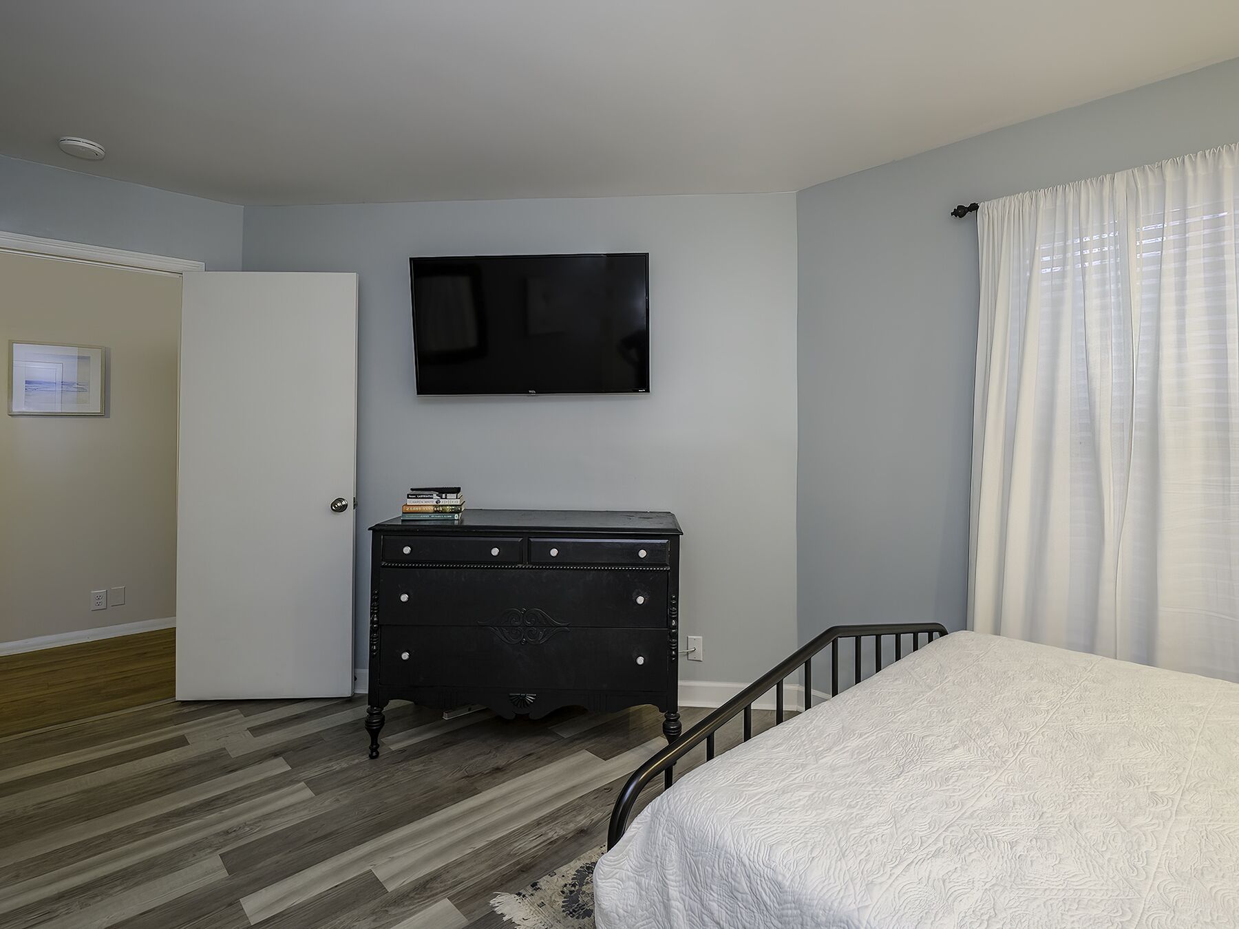 Un dormitorio con una cama, un tocador, un televisor en la pared y una puerta.