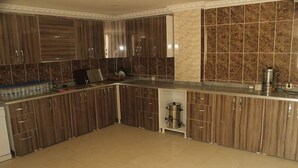 A modern kitchen with dark wooden cabinets, a marble backsplash, and a stainless steel coffee maker on the countertop. - Otel Gerger (Gerger)
