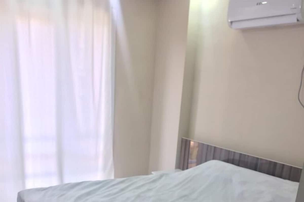 A single bed with a white mattress in a room with a light-colored floor and walls.