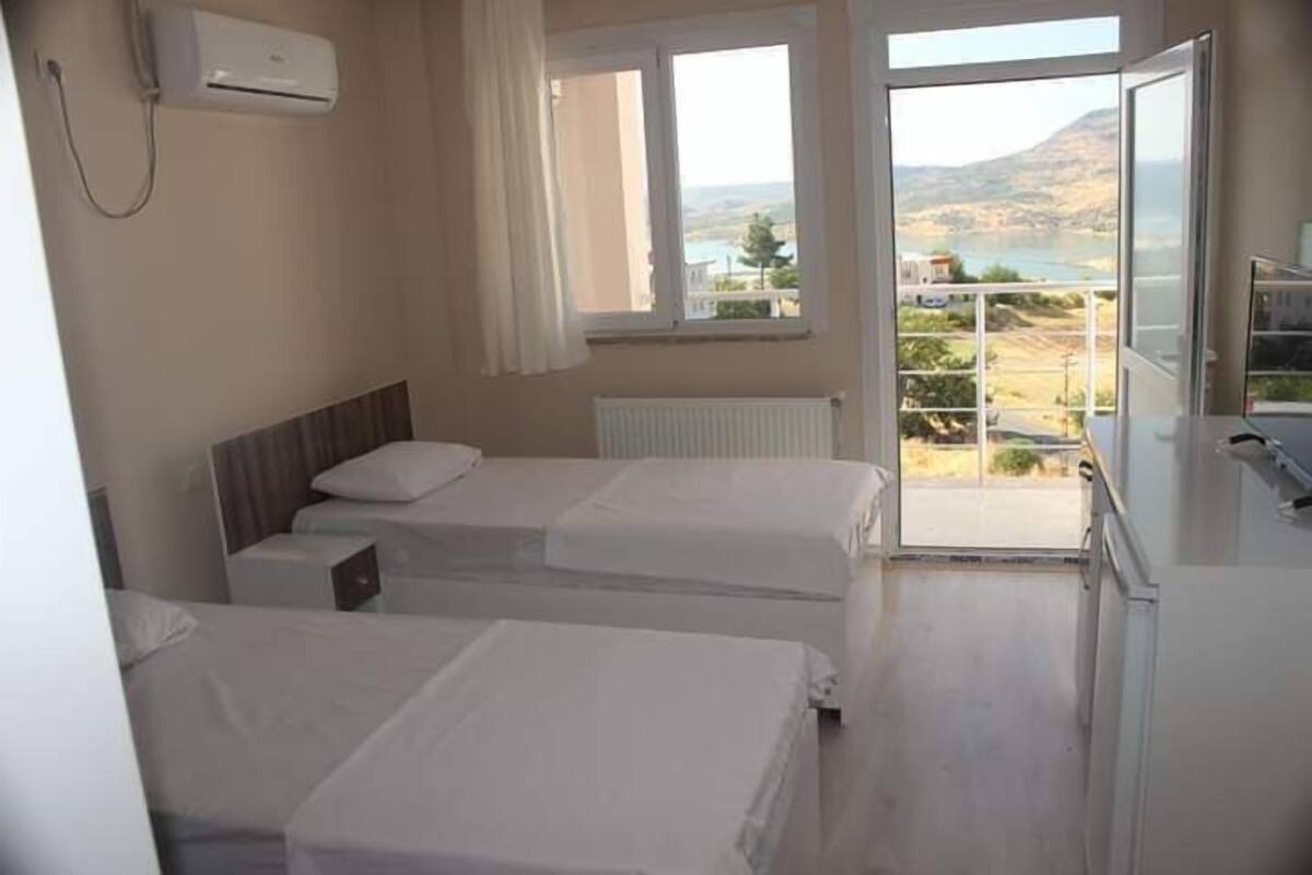 A hotel room with two beds, a window with a view of a landscape, and an air conditioning unit on the wall.