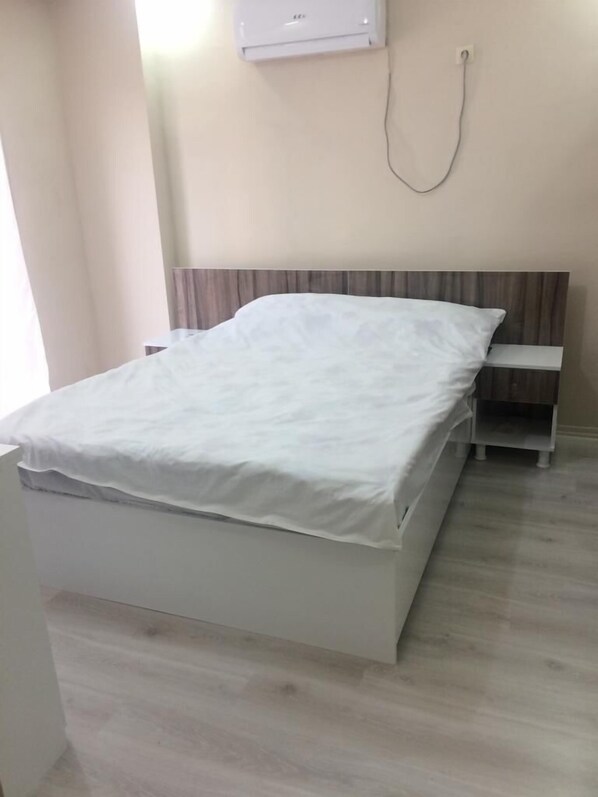 A bedroom with a bed, a bedside table, and a wall-mounted air conditioner.