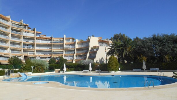 A hotel with a swimming pool, multiple balconies, and lush greenery. - Apartment "Le Jean Bart" with pool and views of Cannes Marina (Mandelieu-la-Napoule)