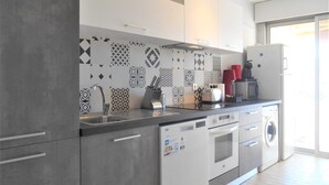 A modern kitchen with grey cabinets, a patterned backsplash, and a built-in dishwasher and oven. - Apartment "Le Jean Bart" with pool and views of Cannes Marina (Mandelieu-la-Napoule)