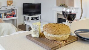 A living room with a television, a fireplace, a glass of red wine, and a loaf of bread on a wooden board.