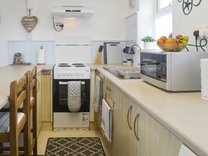 A compact kitchen with a stove, microwave, and toaster. There is a small sink and a fruit bowl on the counter.