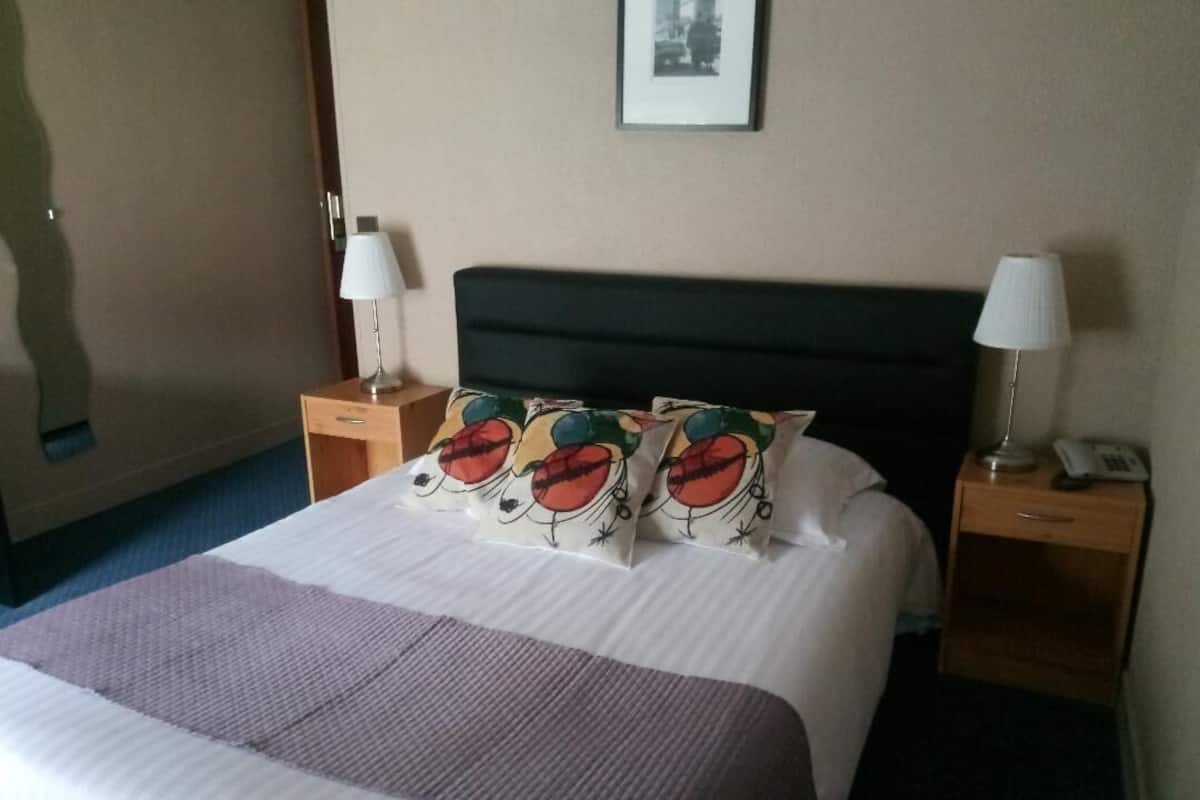 A hotel room with a bed, two bedside tables, and two lamps.