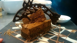 Una porción de pastel de chocolate con glaseado de chocolate blanco sobre un plato de pizarra.