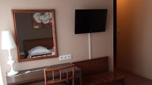 Habitación de hotel con una cama, un escritorio con silla, un televisor y un espejo.