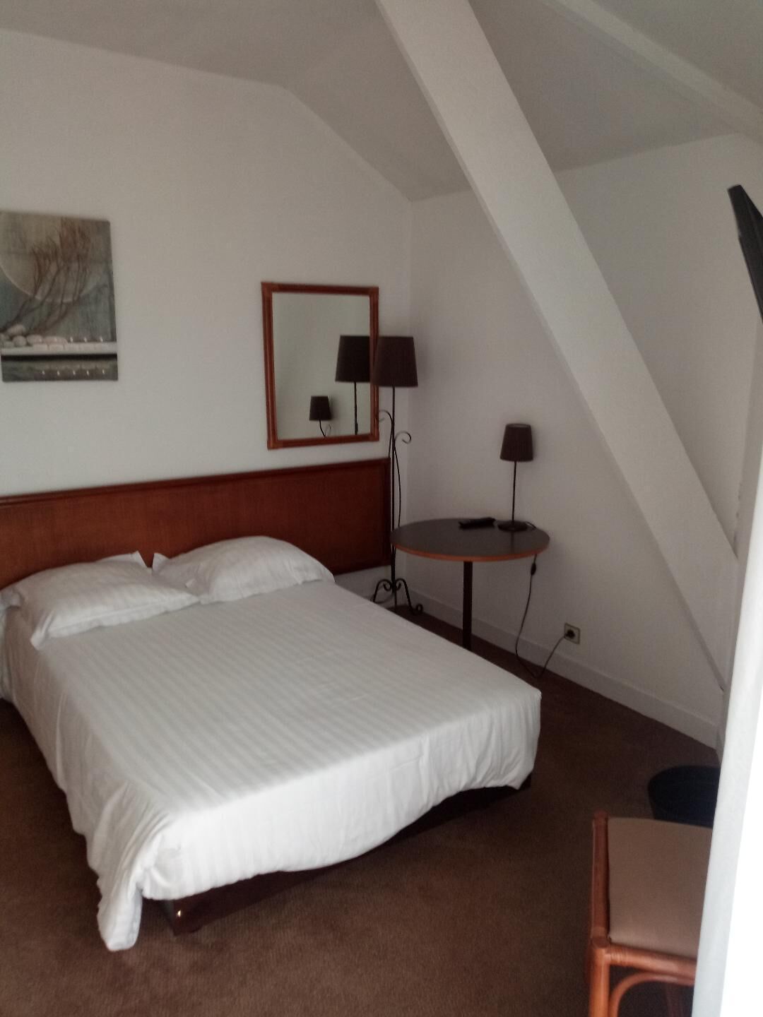 A hotel room with a large bed, a small round table, a desk, and a mirror on the wall.