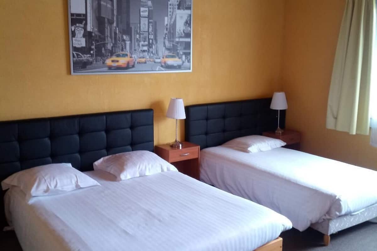 A hotel room with two single beds, a wooden headboard, a cityscape painting on the wall, and a window with curtains.