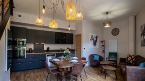 Una cocina moderna con armarios oscuros, una mesa de comedor preparada para cuatro personas y una escalera a la izquierda.