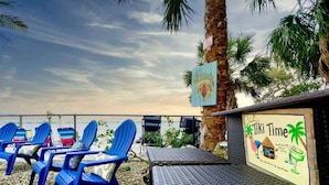 Een zitgedeelte aan het strand met blauwe stoelen en een tafel, een palmpijlstruik en een bord met de tekst 'Tiki Time'.