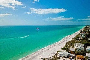 A beach with clear turquoise water, a parasail in the distance, and buildings along the shore. - Waterfront Villa Seaglass wows! Pool & Bayfront (Englewood)