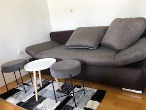A modern living room with a dark grey sofa, two matching armchairs, a small white table, and a black and white rug. - Alher Apartma (Ljubljana)