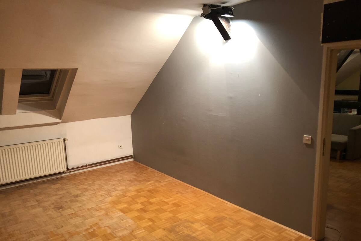 An attic room with a sloped ceiling, a radiator, and a wooden floor.