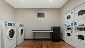 A laundry facility with multiple washing machines and dryers, a small table, and a sign on the wall. - Extended Stay America Premier Suites Bluffton Hilton Head (Bluffton)