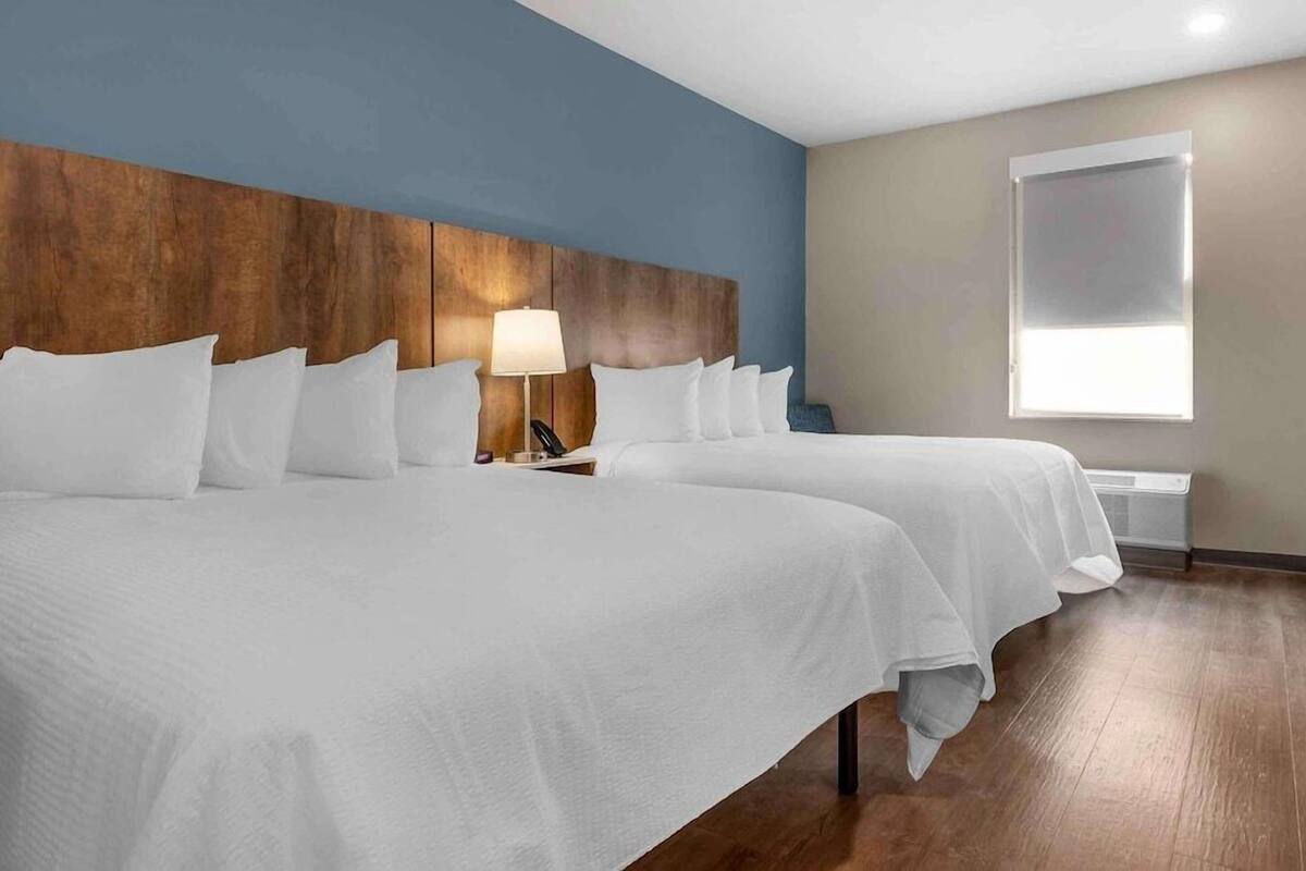 A hotel room with two beds, a wooden headboard, a bedside lamp, a window, and a radiator.