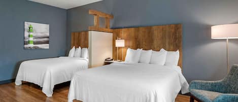 Habitación de hotel con dos camas, cabecero de madera, mesita de noche, lámpara y una silla.
