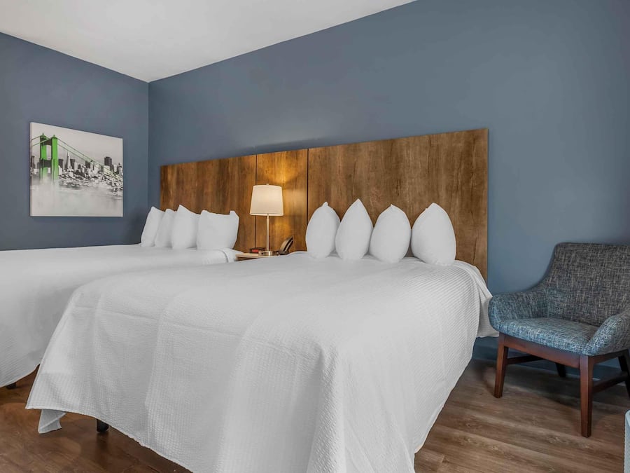 Een hotelkamer met twee bedden, een houten hoofdbord, een lamp, een stoel en een schilderij van een brug.