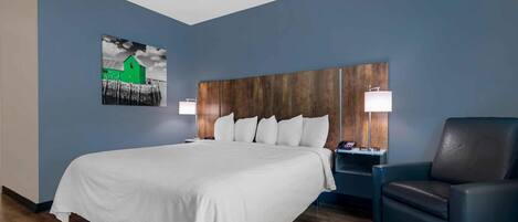 A hotel room with a large bed, a wooden headboard, two bedside tables with lamps, a black leather chair, and a wall-mounted artwork.