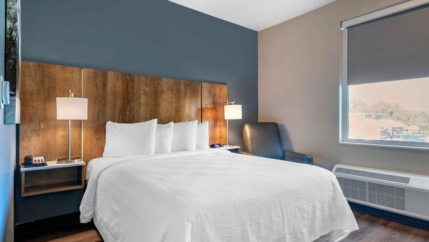 A hotel room with a large bed, two bedside lamps, a nightstand, a chair, a window, and a wall-mounted heater. - Extended Stay America Premier Suites Bluffton Hilton Head (Bluffton)
