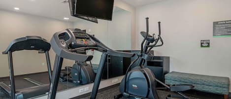 A gym with treadmills, an elliptical, a bench, and a TV mounted on the wall.