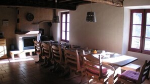 Un comedor rústico con sillas y mesa de madera, una chimenea y lámparas colgantes.