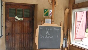 Una puerta de madera rústica con un letrero que indica un restaurante cercano. Una pizarra con un mensaje en francés está colocada sobre un atril de madera.
