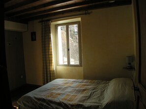 Ein Zimmer mit einem Bett, einem Fenster mit Vorhängen, einem Nachttisch mit einer Lampe und einer Tür.