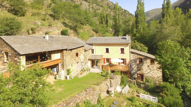 Una casa de piedra rústica con terraza de madera y un pequeño jardín.