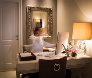 Quarto de hotel com escrivaninha, computador, luminária e espelho.
