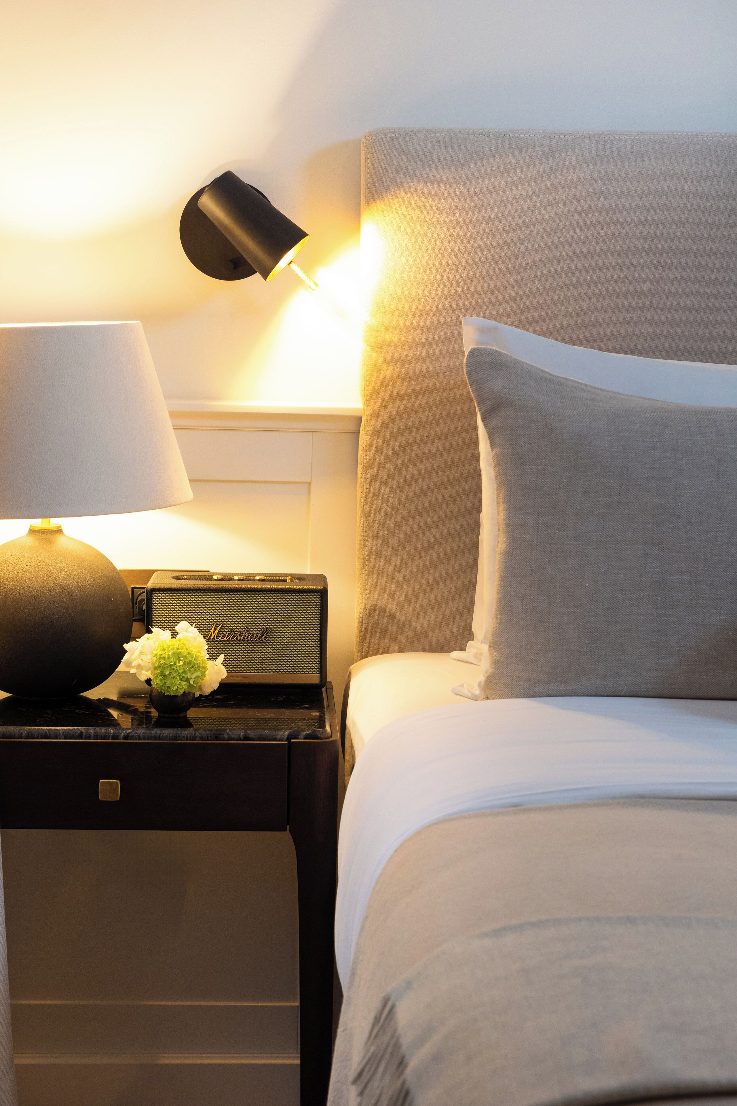A neatly made bed with a pillow, a lamp, and a small speaker on a bedside table.