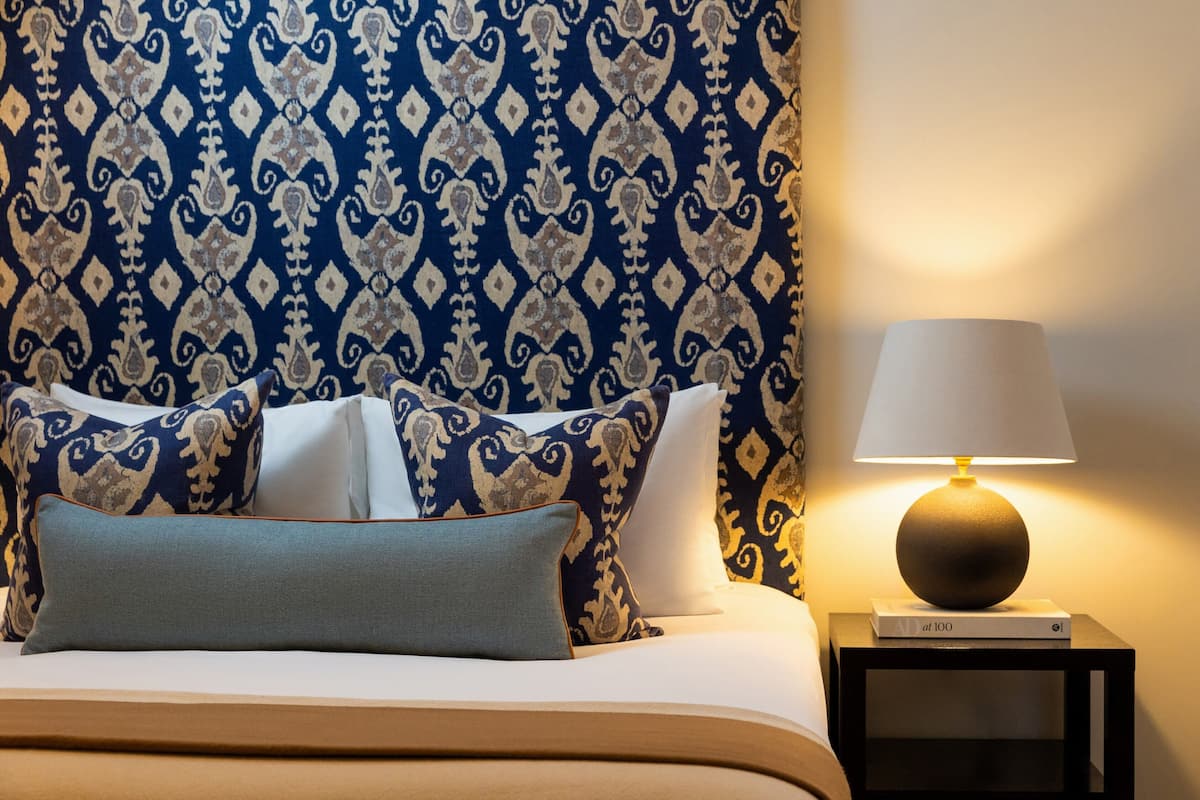A neatly made bed with patterned pillows and a bedside lamp on a nightstand.