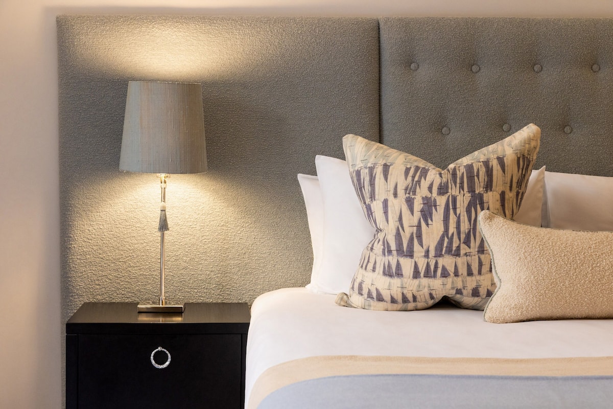 A neatly made bed with patterned pillows and a bedside lamp on a black nightstand.