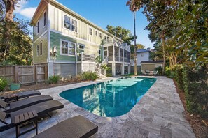 Ein zweistöckiges Haus mit Swimmingpool, Holzterrasse und umzäunter Garten.