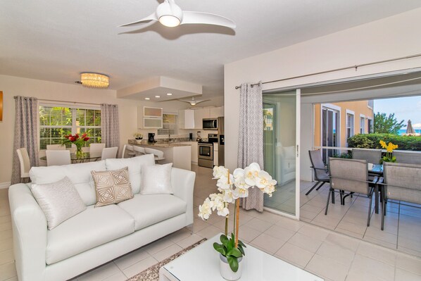 A modern living room with a white sofa, a dining area with a table and chairs, and a kitchen in the background.